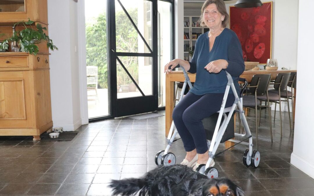 Woman uses a walker while a dog looks on.