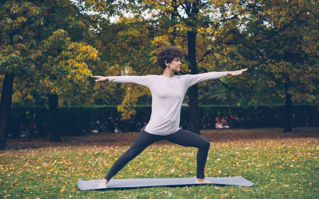 Woman practicing yoga warrior pose in autumn park.